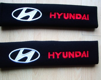 A pair of beautifully embroidered Hyundai soft seat belt covers