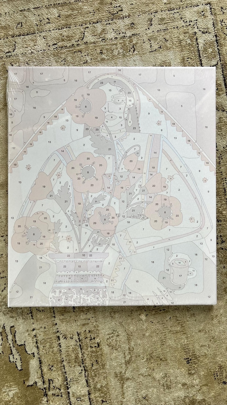 May include: A paint-by-numbers canvas featuring a floral still life. The design includes a vase of flowers with a woman's face in the background. The color palette is soft, with shades of pink, beige, and gray. The canvas is wrapped in clear plastic.