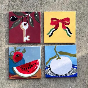 May include: Four square paintings with vibrant designs. One depicts a key on a burgundy canvas, another a red bow on yellow, a watermelon slice and poppy, and a white fruit with a blue backdrop.