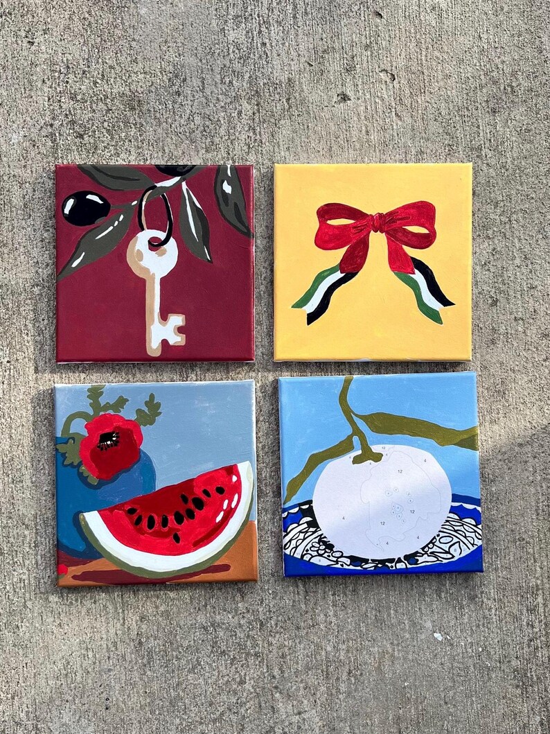 May include: Four square paintings with vibrant designs. One depicts a key on a burgundy canvas, another a red bow on yellow, a watermelon slice and poppy, and a white fruit with a blue backdrop.