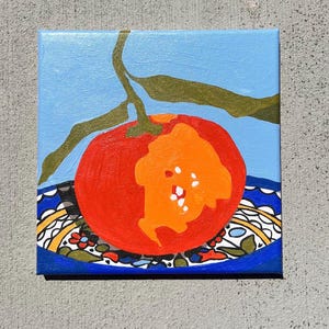May include: A square canvas painting depicting a red tomato with an orange section, set on a blue plate with a patterned border. A green stem and leaves are above against a light blue backdrop. The artwork is a still life, suitable for kitchen decor.