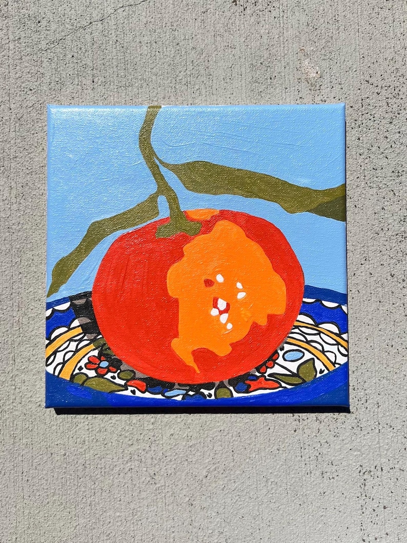May include: A square canvas painting depicting a red tomato with an orange section, set on a blue plate with a patterned border. A green stem and leaves are above against a light blue backdrop. The artwork is a still life, suitable for kitchen decor.