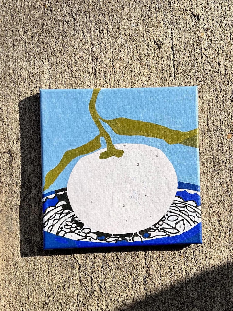 May include: Square canvas art depicting a white fruit with a green stem and leaves against a light blue backdrop. The fruit has numbers for paint-by-number. The bottom border has a blue and white patterned design.