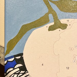 May include: A paint-by-numbers canvas in progress. The image shows a light blue background, a white shape, and olive green branches. The lower left corner has a blue and black patterned design. Numbers are visible within the white shape.
