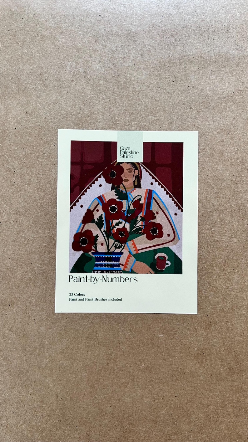May include: A paint-by-numbers kit featuring a floral design. The artwork depicts a woman with flowers in a vase, a cup, and the text "Gaza Palestine Studio". The kit includes 23 colors and paint brushes.