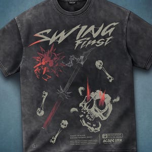 Puede incluir: Una camiseta de manga corta gris carbón con efecto lavado. El frente presenta el texto "SWING First" en una fuente estilizada, una maza roja con púas, una calavera con ojos rojos brillantes y dos llaves. Texto adicional incluye "FORGED IN BLOOD" y "SCAPE INK".