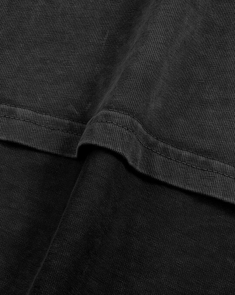 The image is a close-up of a dark grey fabric, possibly a piece of clothing or a textile. The fabric appears to be made of a woven or knitted material, with a textured and slightly wrinkled appearance.