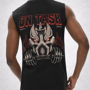 Op de afbeelding: Zwart mouwloos shirt met een grafisch ontwerp op de rug. Het ontwerp toont een gestileerd metalen gezicht met rode ogen, vlammen en de tekst "ON TASK" in rood. Daaronder staat de tekst "ASSIGNED TO SUFFER".