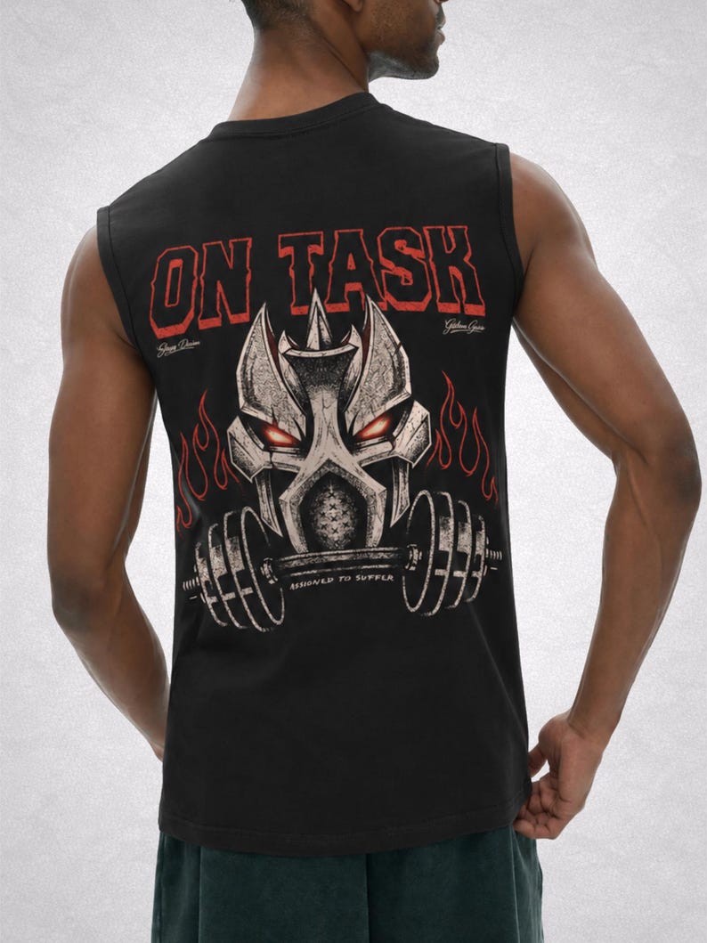 Op de afbeelding: Zwart mouwloos shirt met een grafisch ontwerp op de rug. Het ontwerp toont een gestileerd metalen gezicht met rode ogen, vlammen en de tekst "ON TASK" in rood. Daaronder staat de tekst "ASSIGNED TO SUFFER".