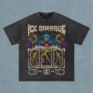 May include: A charcoal grey acid-wash t-shirt featuring a graphic print with the text ICE BARRAGE. The design displays a blue-robed figure above three framed skeletons, with small circular icons at the bottom including a skull and crossbones.