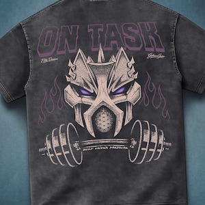 Pode incluir: Uma t-shirt cinza-carvão com uma estampa gráfica de um capacete estilizado com olhos roxos acima de uma barra de pesos. O texto "ON TASK" aparece no topo em roxo, com "Elite Division", "Gains" e "BUILT UNDER PRESSURE" em branco.