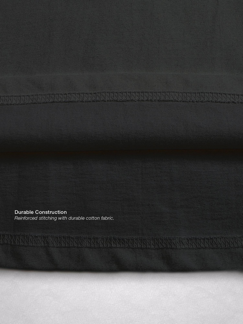 Op de afbeelding: Close-up van een donkergrijze stof met zichtbare stiksels. De tekst "Durable Construction" en "Reinforced stitching with durable cotton fabric" is op de stof gedrukt. De afbeelding benadrukt de constructie van het kledingstuk.