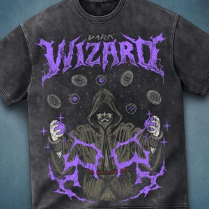 Peut inclure: Un t-shirt gris anthracite à manches courtes avec une impression graphique représentant une silhouette encapuchonnée en robe. Le texte "DARK WIZARD" apparaît en violet au-dessus de la silhouette, entourée de jetons flottants et d'éclairs violets.