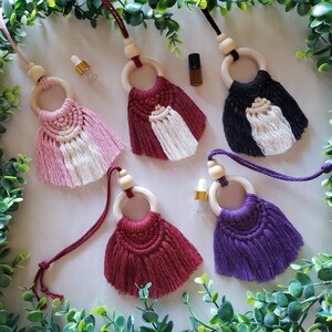 Peut inclure: Cinq diffuseurs d'air de voiture faits à la main avec des anneaux en bois et des pompons en macramé colorés. Les pompons sont dans les tons rose, blanc, rouge, noir et violet.