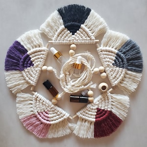 Może przedstawiać: Kolekcja ręcznie robionych makramowych dekoracji ściennych w kształcie gwiazdy, każda z innym akcentem kolorystycznym: fioletowym, różowym, bordowym, szarym i czarnym. W zestawie małe szklane butelki i drewniane koraliki.