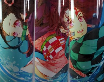 May include: Two anime characters, a girl with pink hair and a boy with green hair, are depicted on a stainless steel tumbler. The girl is wearing a pink and white checkered kimono, and the boy is wearing a green and black checkered kimono. They are both surrounded by blue water.