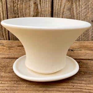 Puede incluir: Una maceta de cerámica color crema con la parte superior acampanada y un platillo a juego. La maceta tiene un acabado liso y mate y un diseño simple y elegante. Adecuada para plantas pequeñas y suculentas.