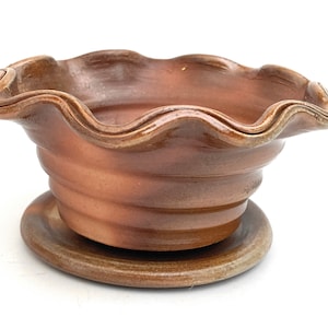 Può includere: Un vaso di terracotta marrone con un bordo ondulato e un sottovaso abbinato. Il vaso ha una finitura testurizzata e smaltata.