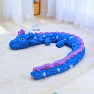 May include: A blue and purple crocheted dragon plush toy with white stars. The dragon is curled up in a circle.