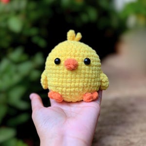 Könnte beinhalten: Ein kleines gelbes Häkeltier in Form eines Kükens mit schwarzen Augen, einem orangefarbenen Schnabel und orangefarbenen Füßen.