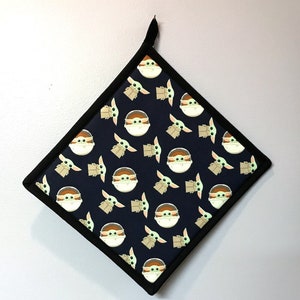 May include: A black and green pot holder with a repeating pattern of a cartoon character from the Star Wars franchise. The character is green and has large ears and eyes. The character is wearing a brown robe.