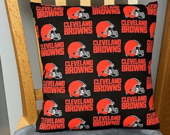 May include: A black and orange pillow with a repeating pattern of the Cleveland Browns logo. The logo features a brown football helmet with a white stripe.