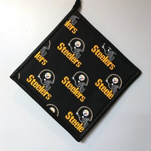 May include: Black square kitchen pot holder with a repeating pattern of yellow "Steelers" text and a black and white football helmet graphic.