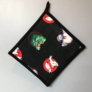 May include: Black square Ghostbusters pot holder with a black border and a loop for hanging. The pot holder features the Ghostbusters logo and images of Slimer and the Stay Puft Marshmallow Man.