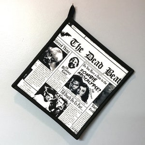 May include: Black and white pot holder with a newspaper design featuring the text "The Dead Beat" and "Do You Have a Date to the Zombie Apocalypse?"  The pot holder has a black border and a black hanging loop.