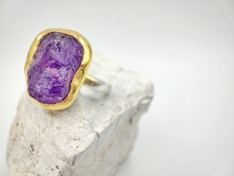 Lovely statement ring for glamorous outfits, featuring a brilliant natural raw amethyst gemstone, coated in 925 sterling silver, with a bezel setting of 18K gold. Minimal aesthetic with a medium, big natural purple amethyst gemstone ring.