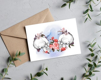Könnte beinhalten: Zwei weiße Schädel mit Blumenarrangements aus rosa und lila Blüten auf einem blauen Aquarellhintergrund.