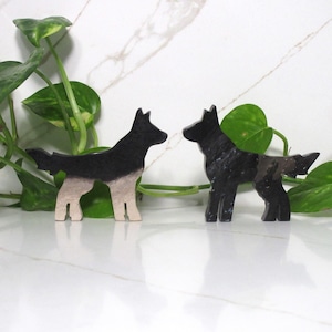 Puede incluir: Dos figuritas de perro de madera, una negra y otra negra y blanca, de pie sobre una superficie de mármol blanco.