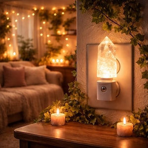 May include: A plug-in wall night light featuring a clear, faceted crystal point as the shade. The light is mounted on a white base with a small circular sensor, emitting a warm, glowing light that illuminates the surrounding textured wall.
