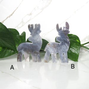 May include: Two gray, iridescent, ceramic reindeer figurines. The reindeer are standing on a white surface. The reindeer on the left is labeled "A" and the reindeer on the right is labeled "B".