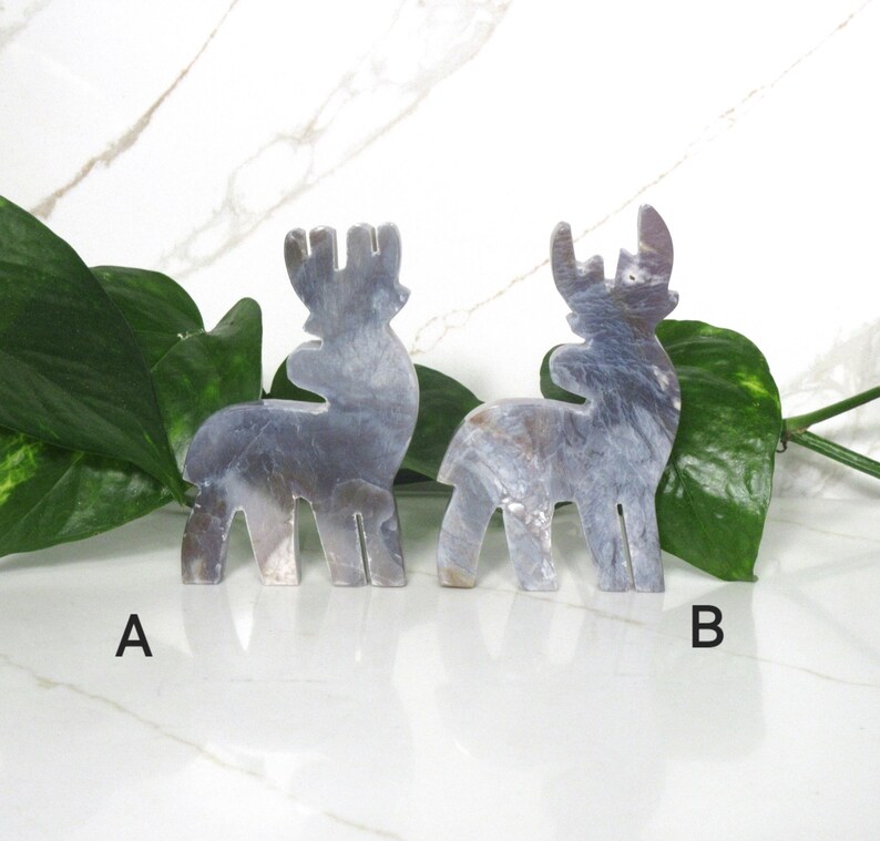 May include: Two gray, iridescent, ceramic reindeer figurines. The reindeer are standing on a white surface. The reindeer on the left is labeled "A" and the reindeer on the right is labeled "B".