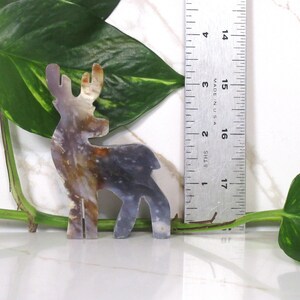 May include: A decorative deer figurine made of agate, with brown, white, and gray colors. The deer is standing on a white surface and is approximately 5 inches tall.