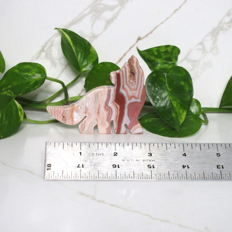 Puede incluir: Una figurita de lobo de &aacute;gata tallada con bandas rosadas, blancas y rojas. La figurita mide aproximadamente 5 cm de alto y est&aacute; sentada sobre una regla.