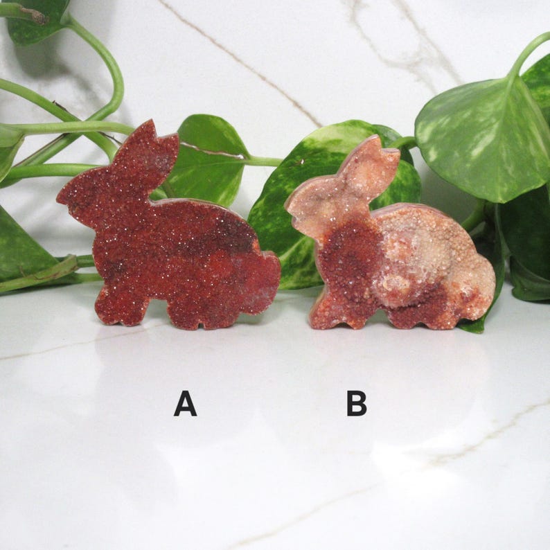 May include: Two decorative bunny figurines. One is a deep red color with a sparkling texture, and the other is a mix of red and tan. The bunnies are side by side, with the letter "A" below the red bunny and "B" below the other.