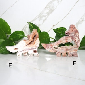 Puede incluir: Dos figuritas de animales talladas en piedra, una blanca con marcas rosas y marrones y la otra rosa con marcas blancas y marrones. Las figuritas tienen forma de zorros y est&aacute;n de pie sobre una superficie de m&aacute;rmol blanco.