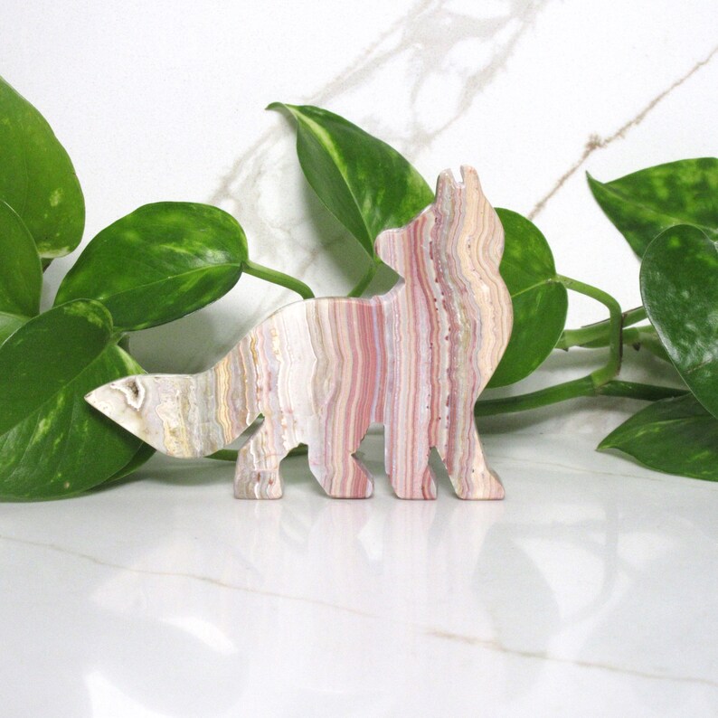 Puede incluir: Una figurita de zorro de &oacute;nix rayada en rosa y blanco. La figurita est&aacute; tallada en una sola pieza de &oacute;nix y tiene un dise&ntilde;o detallado.