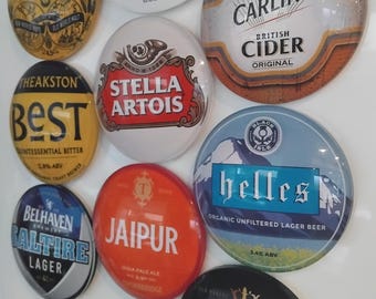 May include: A collection of various beer and cider labels, including "Grolsch," "Carling," and "Stella Artois." The labels are oval-shaped with colorful designs and text, showcasing different brands and styles.