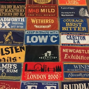 Może przedstawiać: Kolekcja prostokątnych ręczników barowych z różnymi logotypami browarów i nazwami marek, w tym Stella Artois, Carling, Theakston i London 2000. Ręczniki są ułożone w siatkę, prezentując różnorodne kolory, takie jak czerwony, niebieski, czarny i żółty.