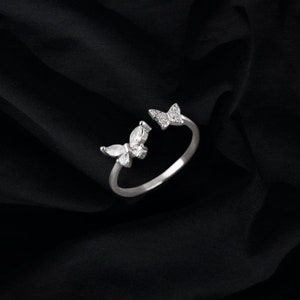 May include: A silver ring with two butterfly designs, each with clear crystal accents.