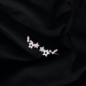 May include: A silver ear cuff with a row of five star-shaped charms, each adorned with clear cubic zirconia stones.