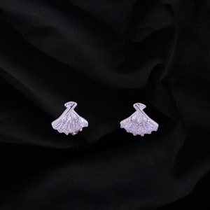 May include: A pair of silver earrings with a fan-shaped design, featuring clear cubic zirconia stones.