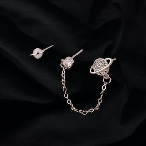 May include: A silver chain earring set with a small crystal and a larger crystal in the shape of a planet with a ring around it.