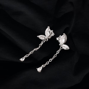 May include: A pair of silver dangle earrings with a butterfly design and clear crystal accents. The earrings have a delicate chain that hangs down from the butterfly.