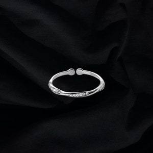 May include: A silver ring with a twisted band and small clear stones set in the band.