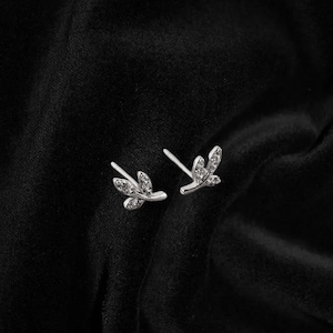 May include: A pair of silver earrings with a delicate leaf design. Each leaf is adorned with small, clear cubic zirconia stones.