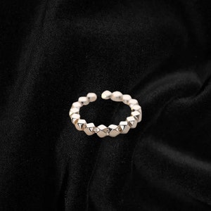 May include: A silver ring with a geometric design. The ring is made up of a series of small, pointed shapes.